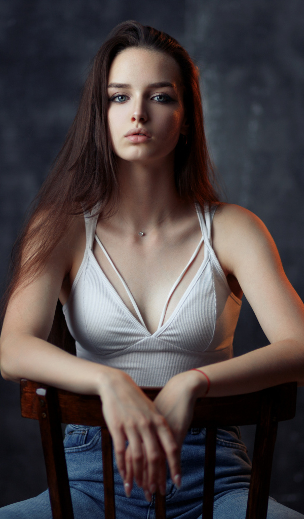 Молодая длинноволосая девушка сидит на деревянном стуле