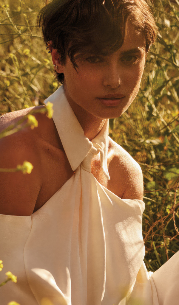 Модель Тейлор Хилл в белом наряде сидит на траве