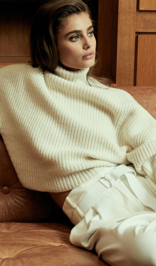 Модель Тейлор Хилл в белом костюме сидит на диване