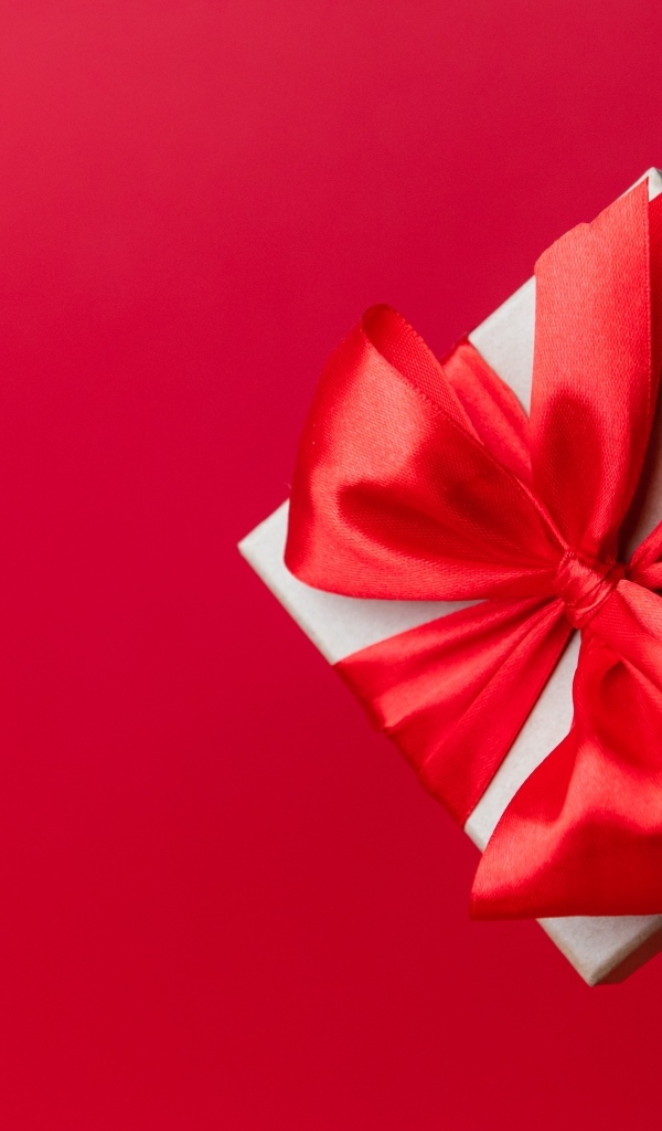 Подарок с бантом из атласной ленты на красном фоне