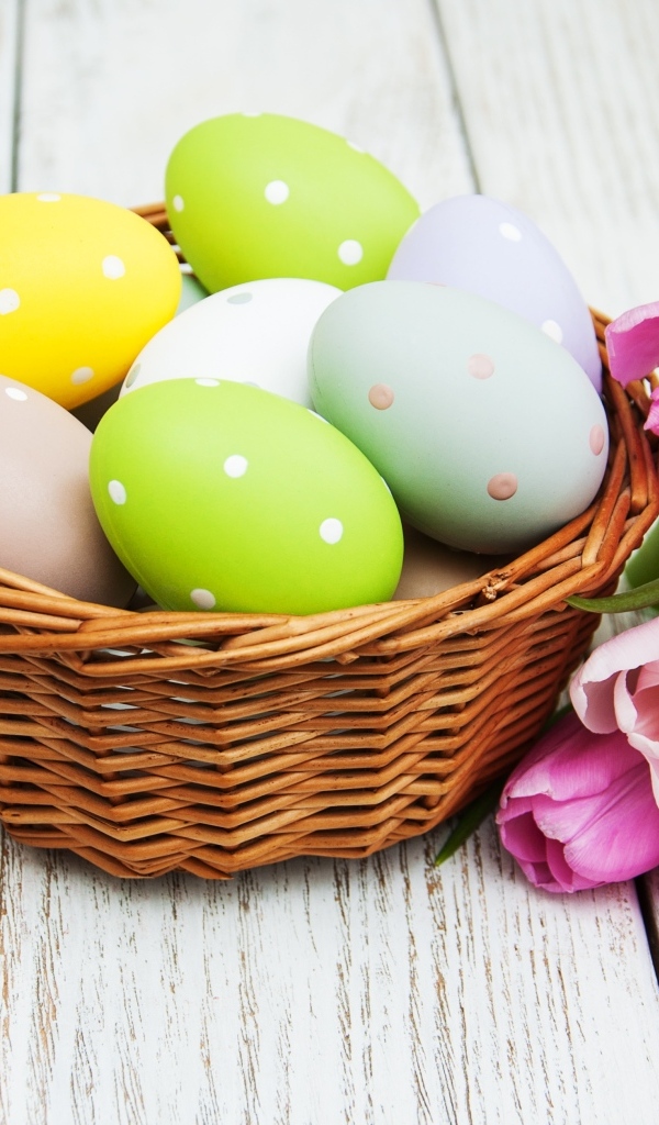 Корзина разноцветных яиц с тюльпанами на столе на Пасху