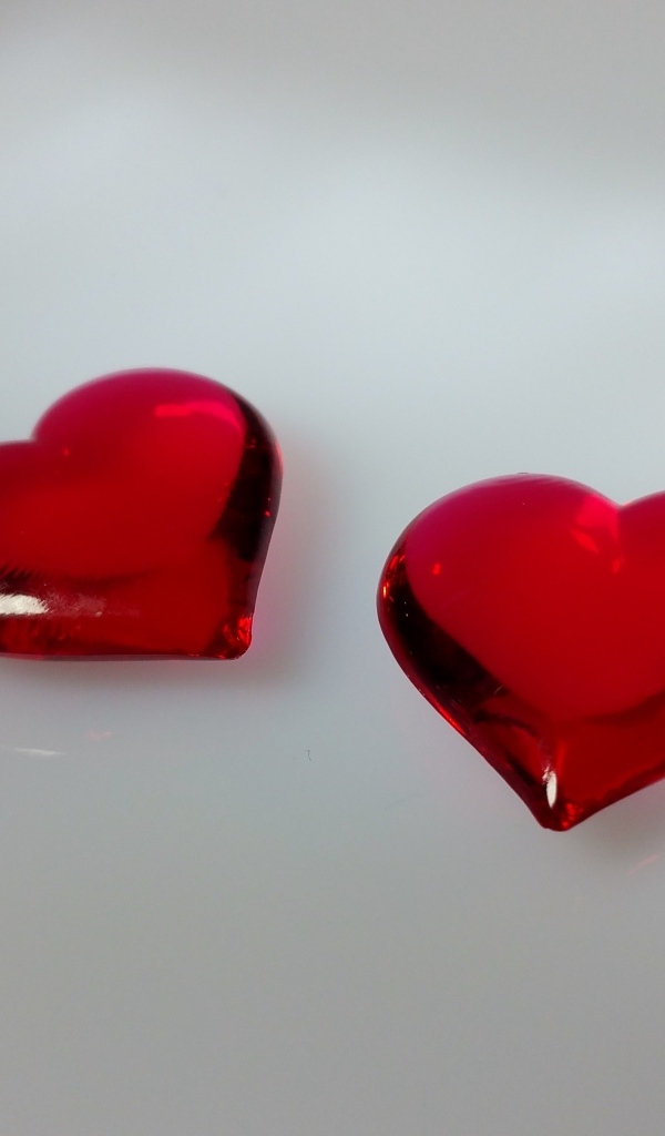 Два красных стеклянных сердца на сером фоне