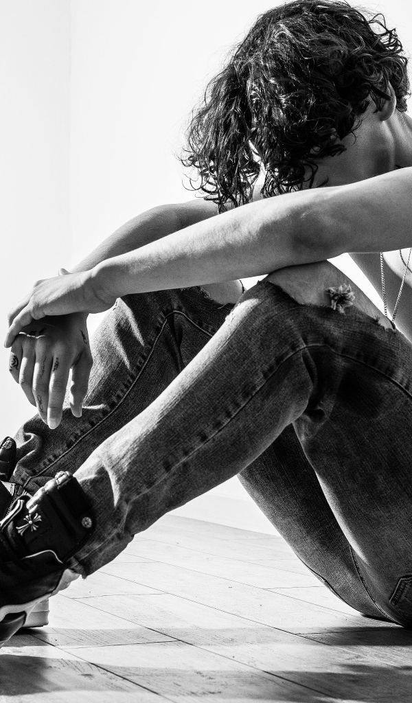 Грустный мужчина в джинсах сидит на полу