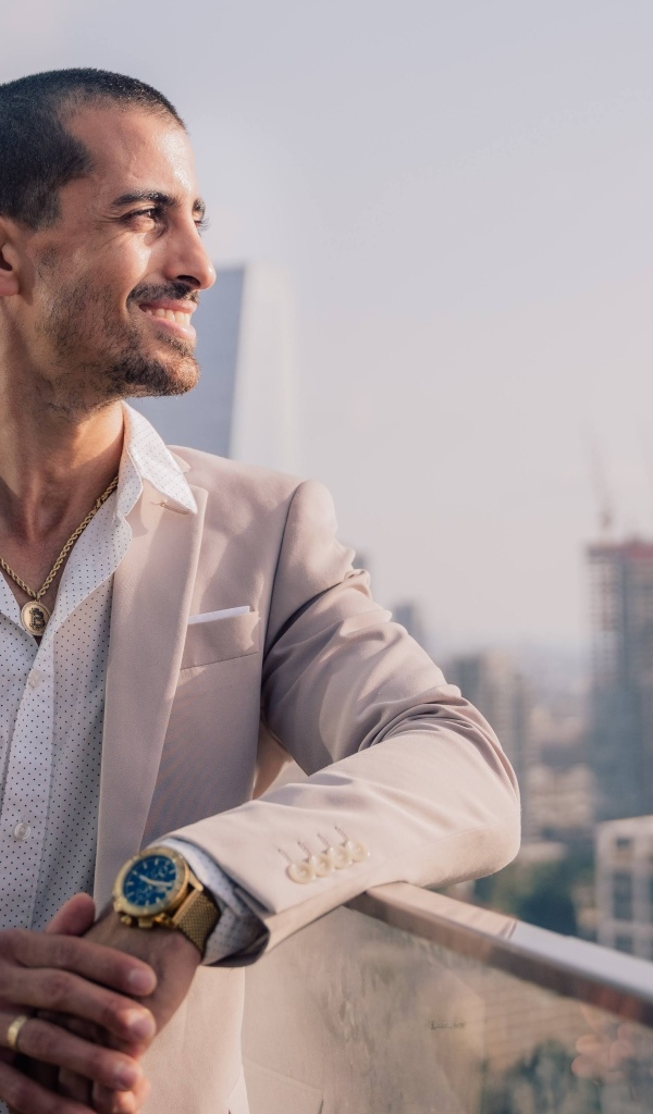 Улыбающийся стильный мужчина в костюме стоит на балконе 