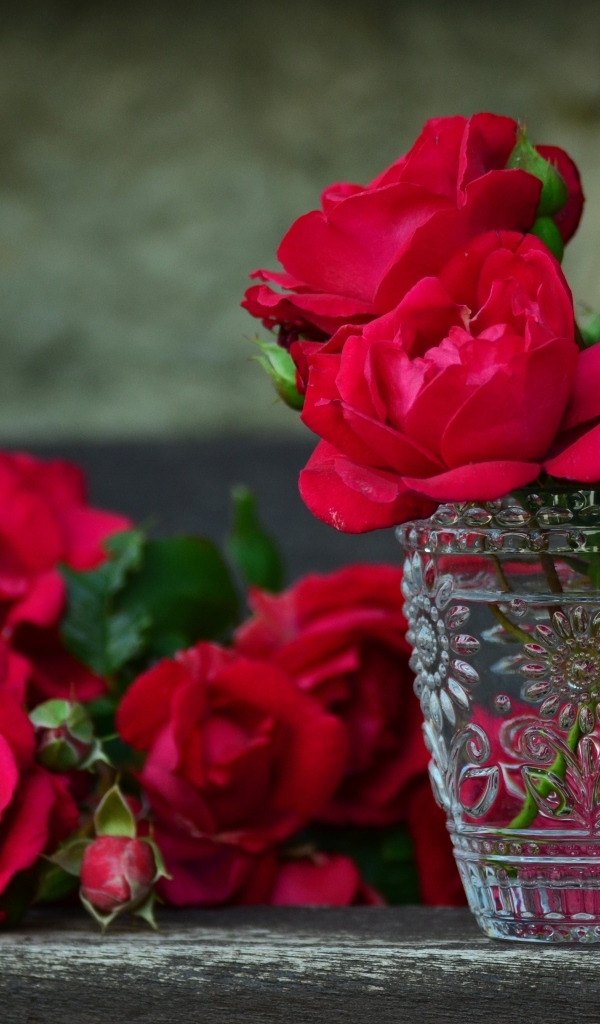 Красные срезанные розы со стеклянным стаканом на столе