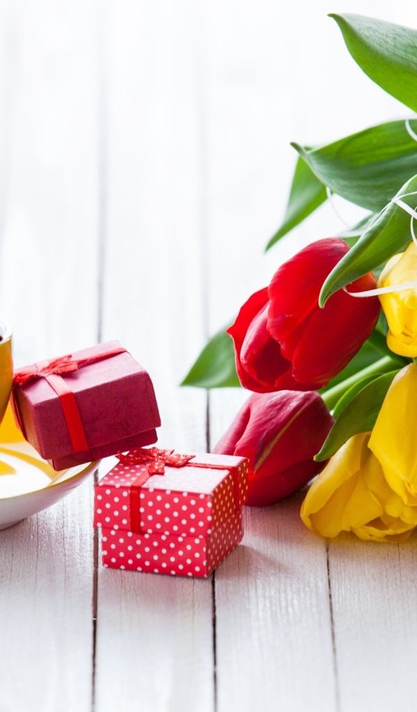 Желтая чашка кофе на столе с подарками и букетом тюльпанов