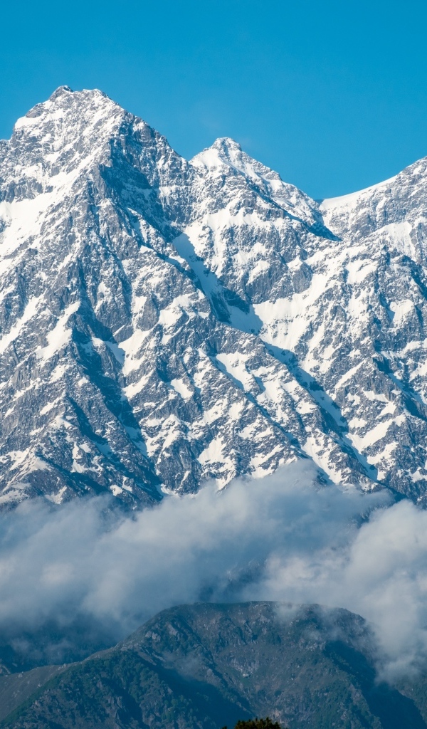 Высокие заснеженные горы в тумане под голубым небом
