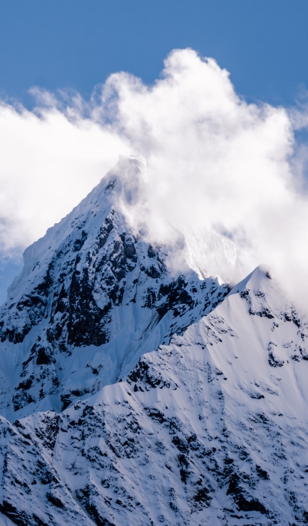 Острая заснеженная вершина горы в белых облаках