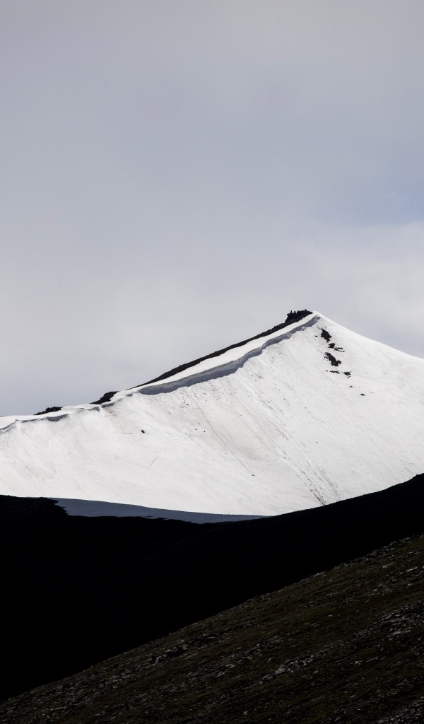 Заснеженная вершина горы под грозовым небом