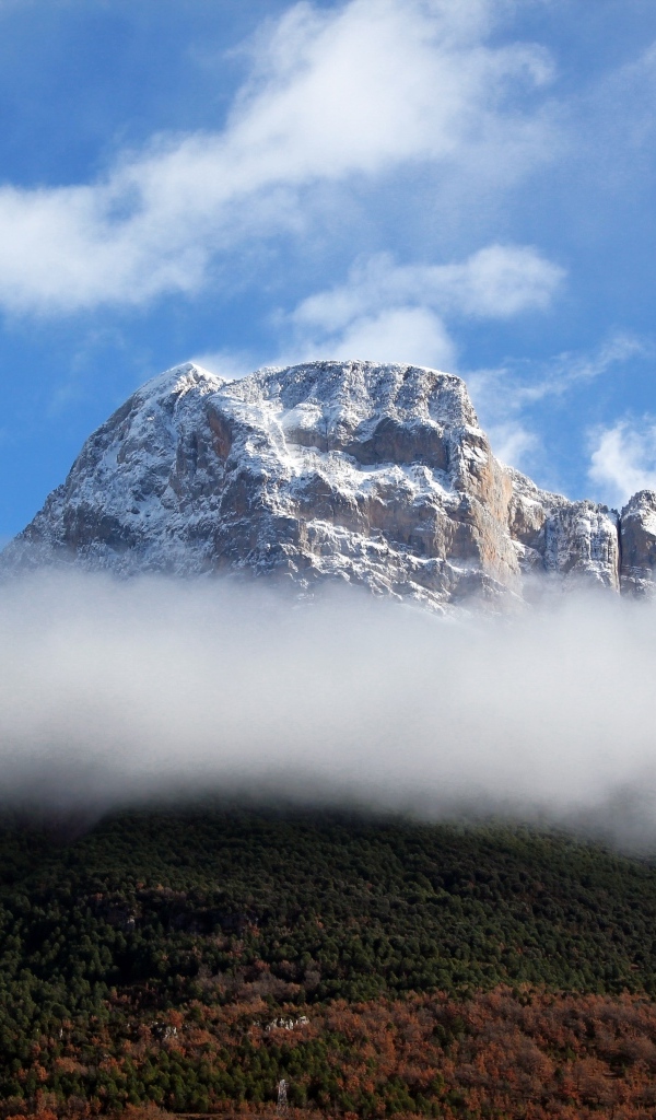 Заснеженная горная вершина в белых облаках