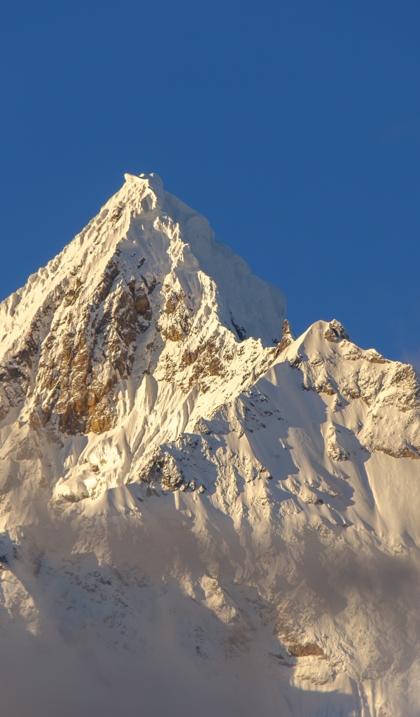 Крутая заснеженная вершина горы на голубом фоне