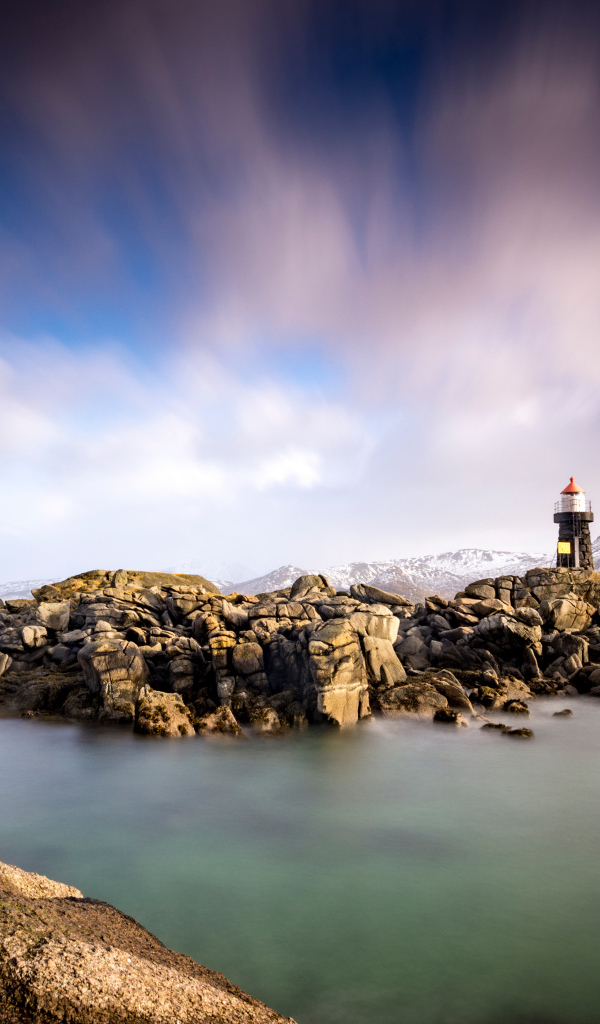 Маяк стоит на каменном берегу на фоне гор