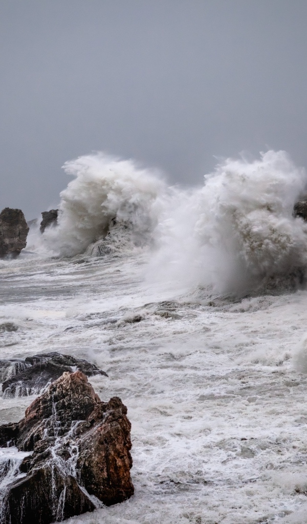 Белые пенные волны бьются об камни во время шторма