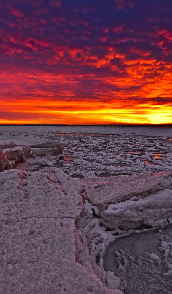 Красный закат солнца покрывает заледеневшее озеро 