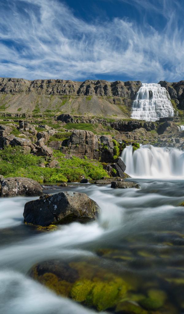 Водопад стекает с гор на фоне красивого голубого неба Исландии