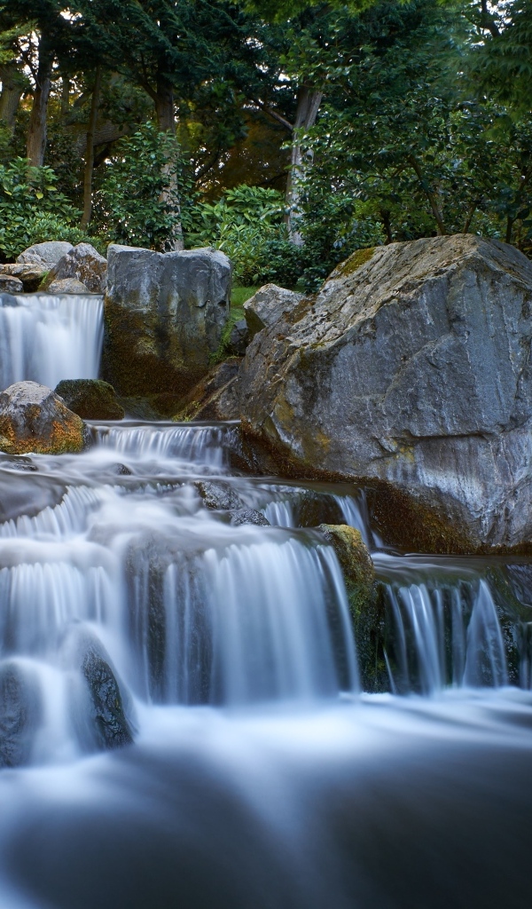 Водопад стекает по большим холодным камням в лесу