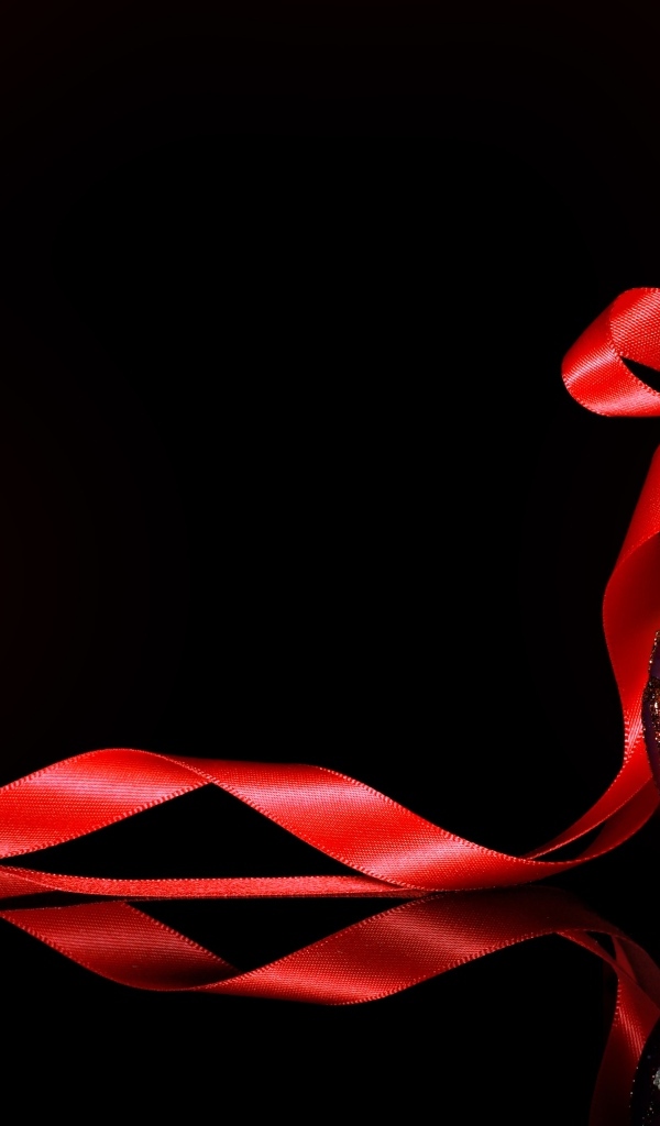 Красный елочный шар с лентой на черном фоне