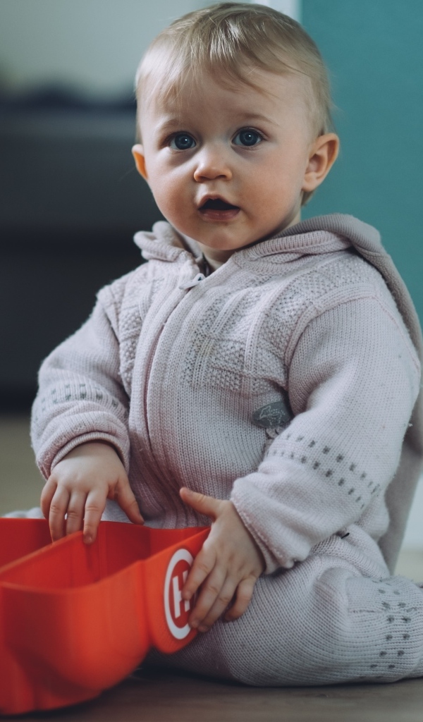 Маленький мальчик в теплом костюме сидит на полу