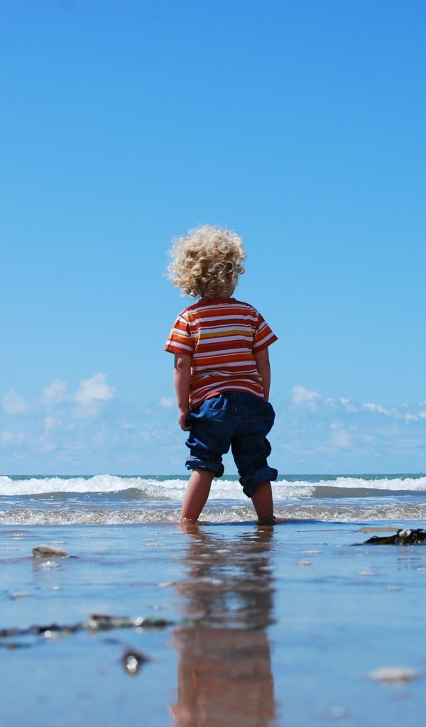 Маленький мальчик гуляет по мокрому песку у моря