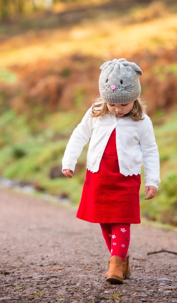 Маленькая девочка в красном платье гуляет по дороге
