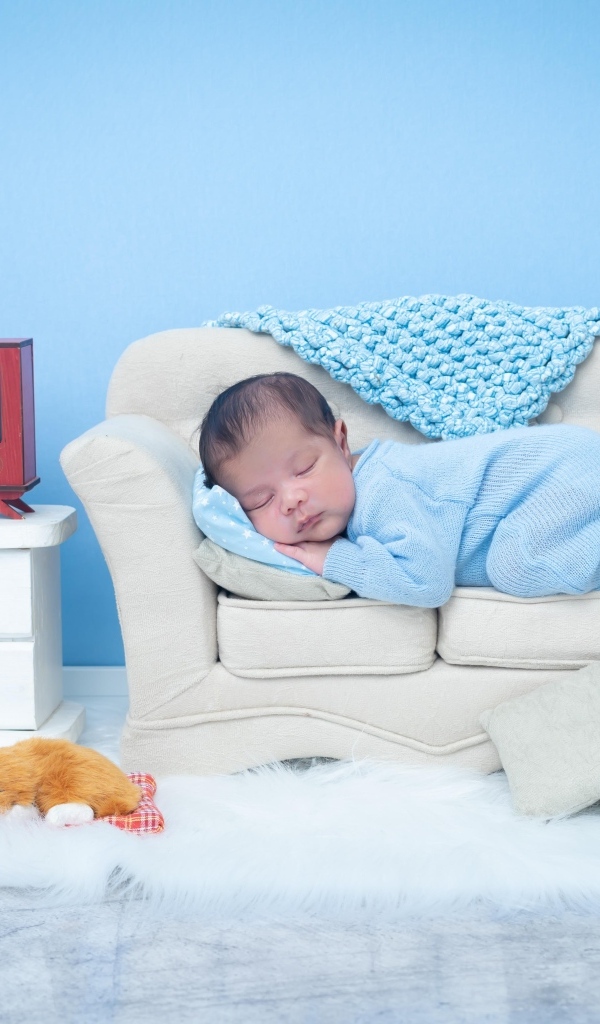 Новорожденный ребенок спит на белом диване на фоне голубой стены