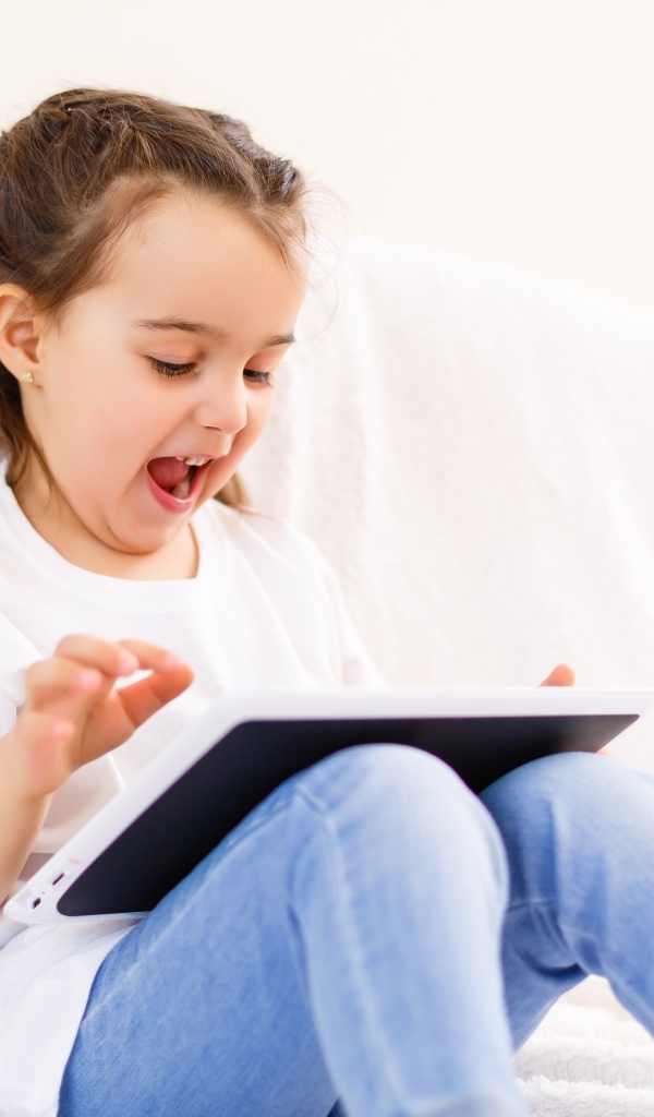 Веселая девочка с планшетом на кровати 
