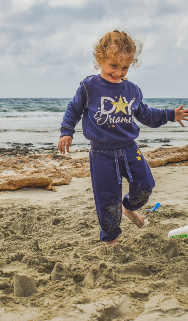 Веселая девочка играет на песке на пляже