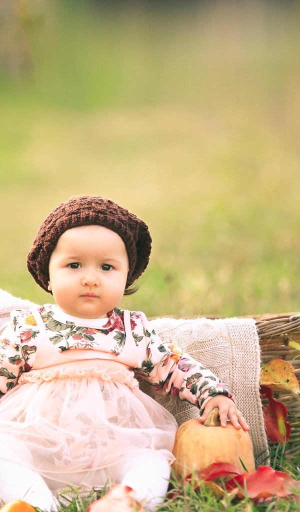 Милая маленькая девочка в шапке сидит на траве 