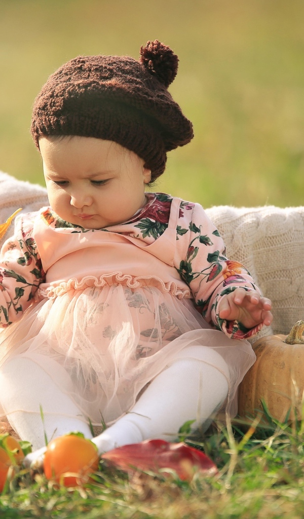 Смешная маленькая девочка сидит на траве с тыквой