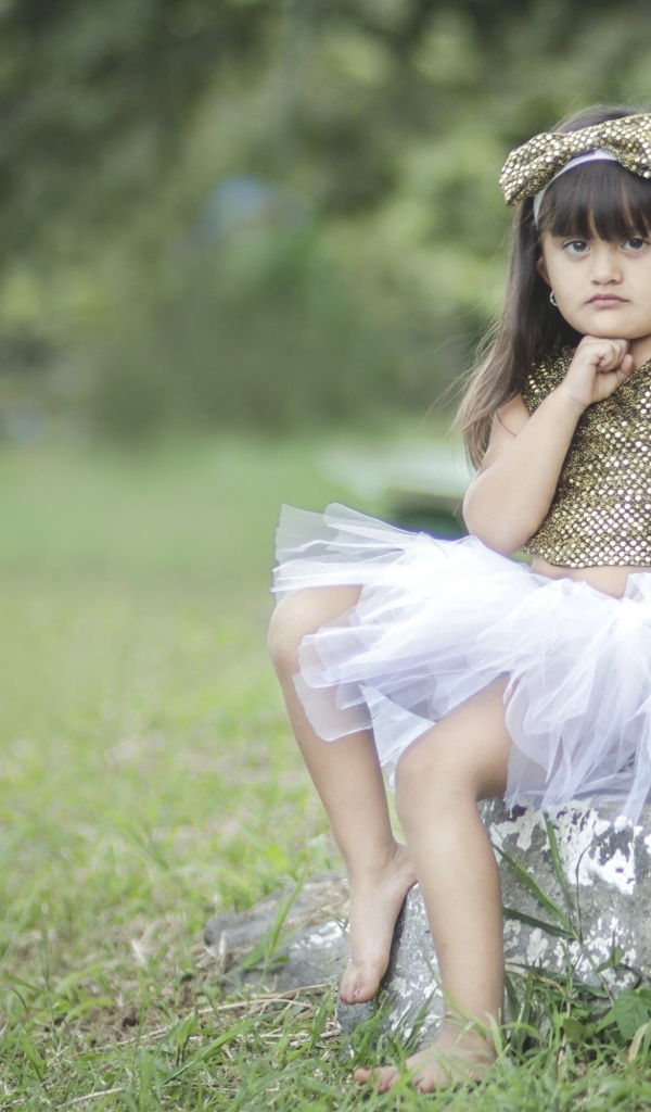 Девочка в красивом платье сидит на камне