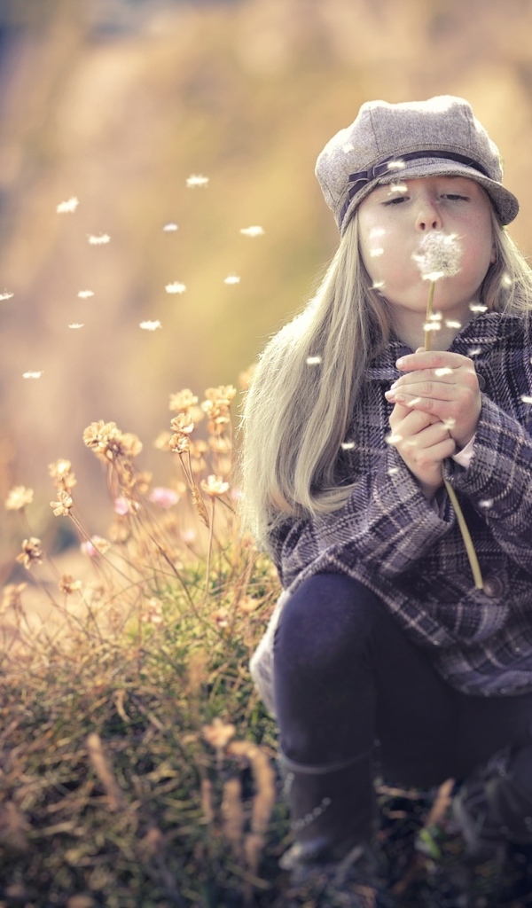 Девочка в кепке сдувает одуванчик