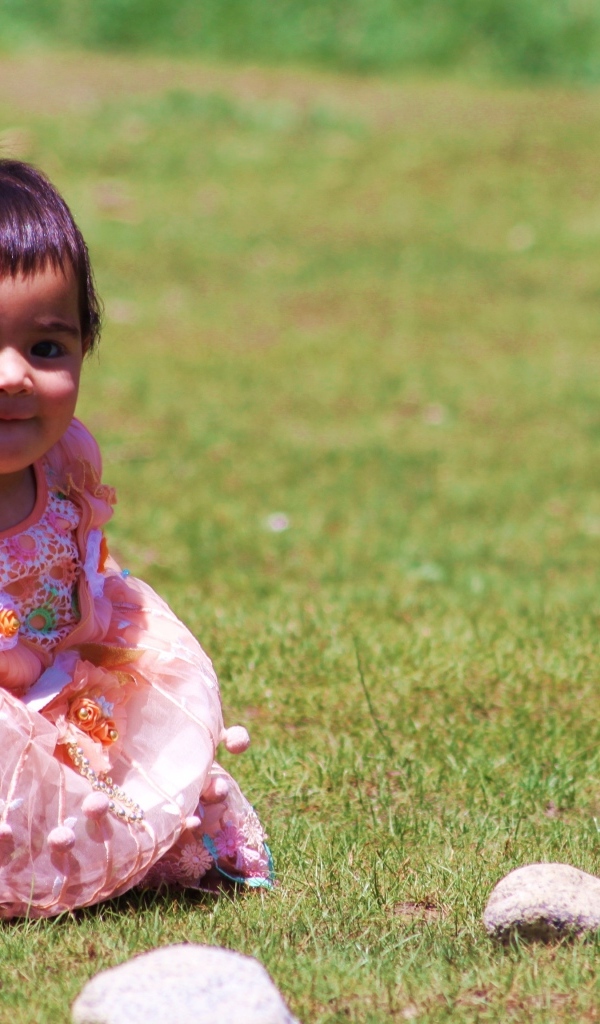Девочка в розовом платье играет на зеленой траве
