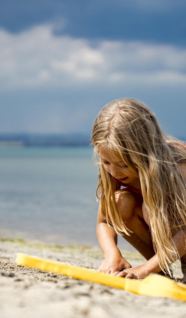 Девочка играет на песке у моря