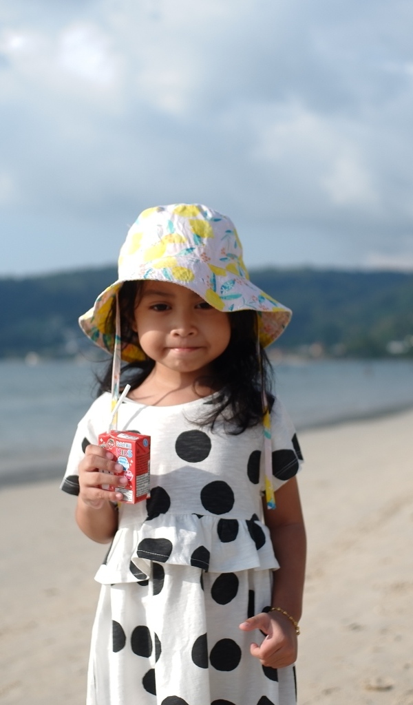 Девочка с соком в руках стоит на пляже