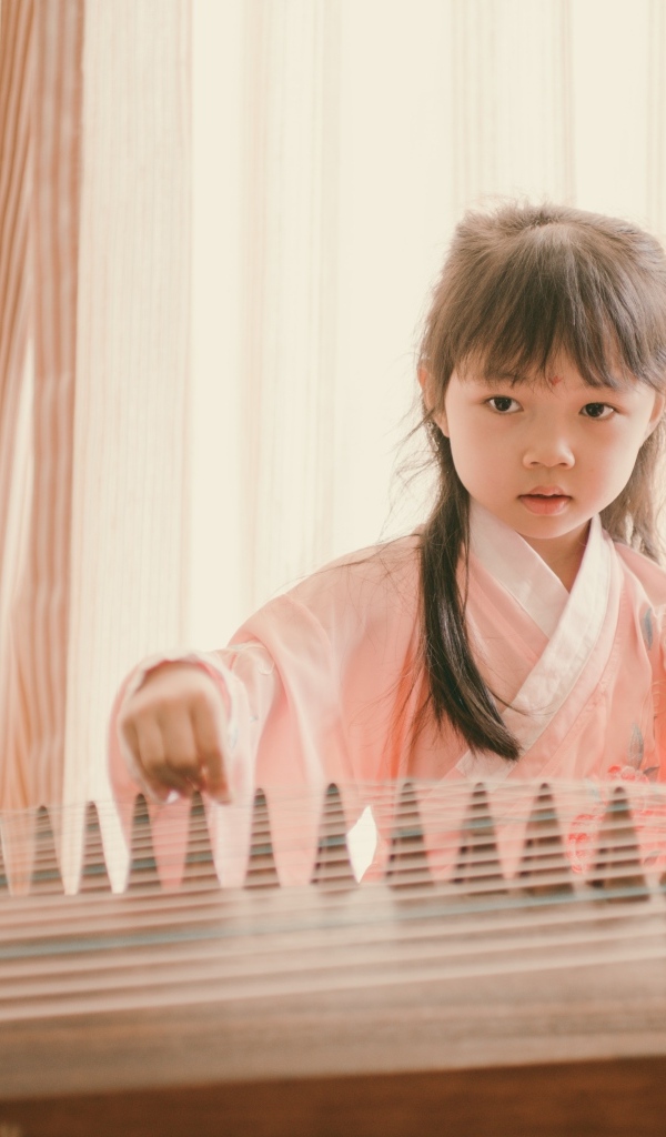 Маленькая девочка азиатка играет на музыкальном инструменте