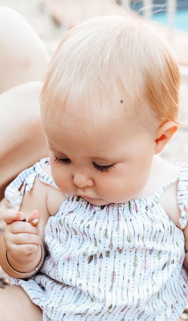 Маленькая светловолосая девочка сидит на песке