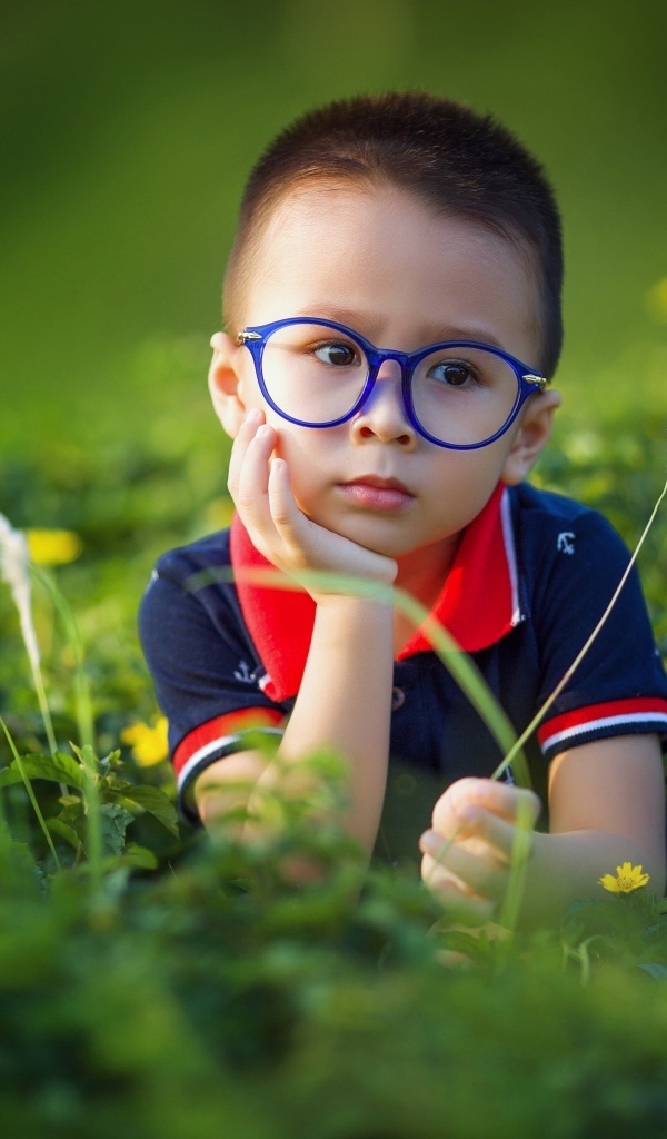Маленький мальчик в очках лежит на траве