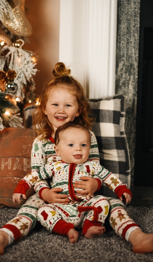 Маленькие брат и сестра сидят у новогодней ели