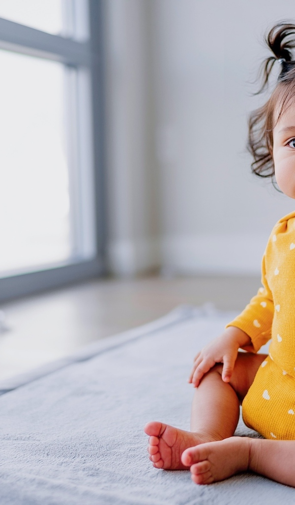 Маленькая смешная девочка сидит у окна