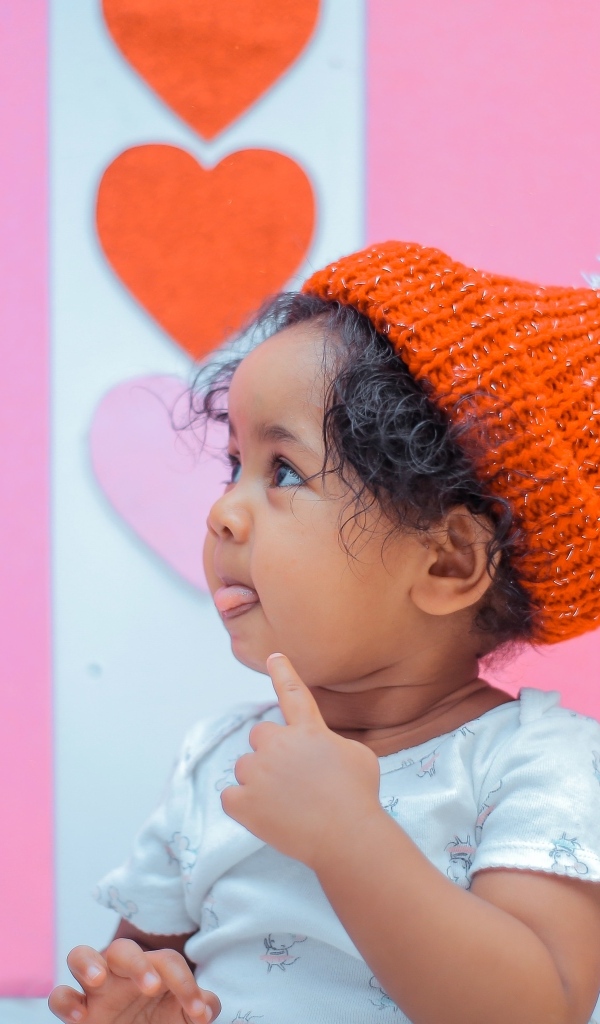 Маленькая девочка в вязаной шапке на розовом фоне