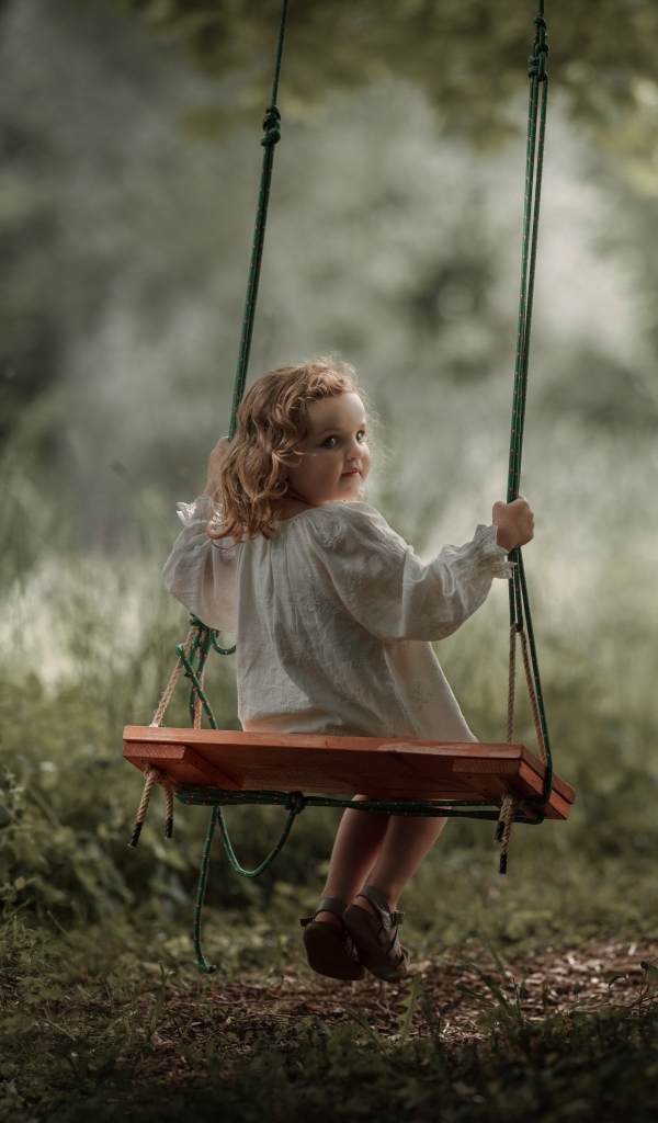 Маленькая девочка на качели в саду