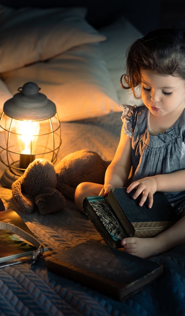 Маленькая девочка читает книги на кровати