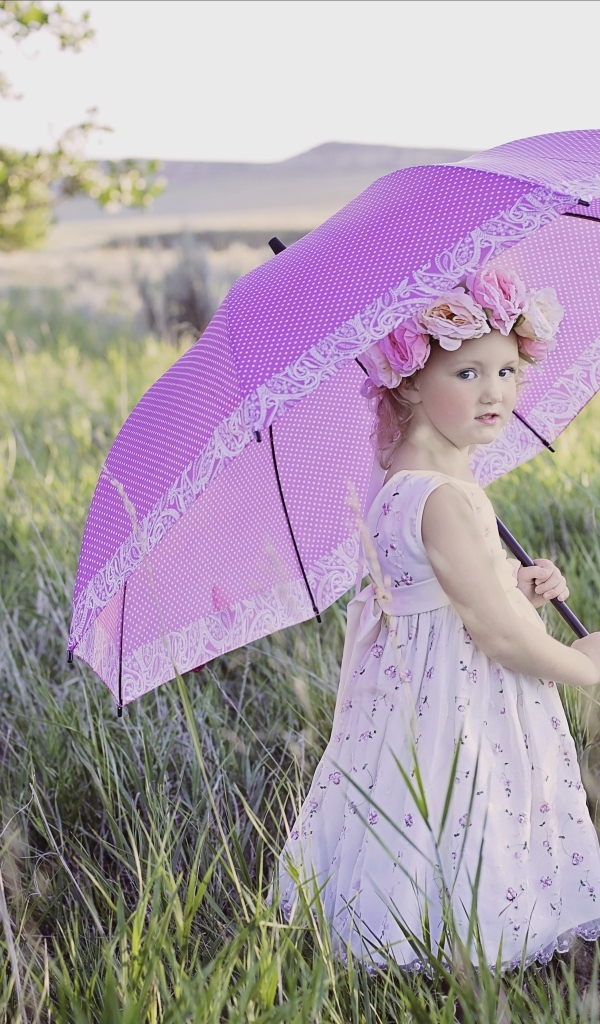 Маленькая девочка стоит в траве с зонтом