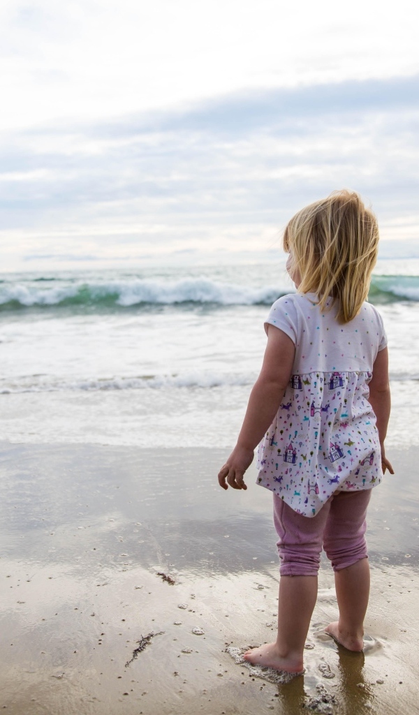 Маленькая девочка стоит на берегу моря