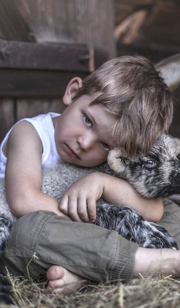 Маленький грустный мальчик обнимает ягненка
