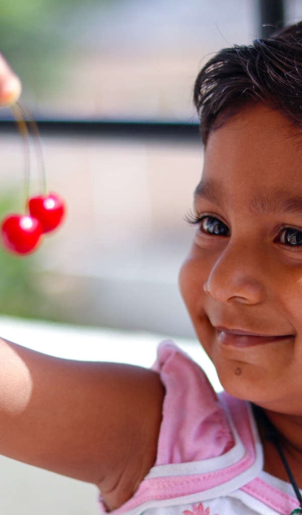 Маленькая улыбающаяся девочка с ягодами вишни в руках