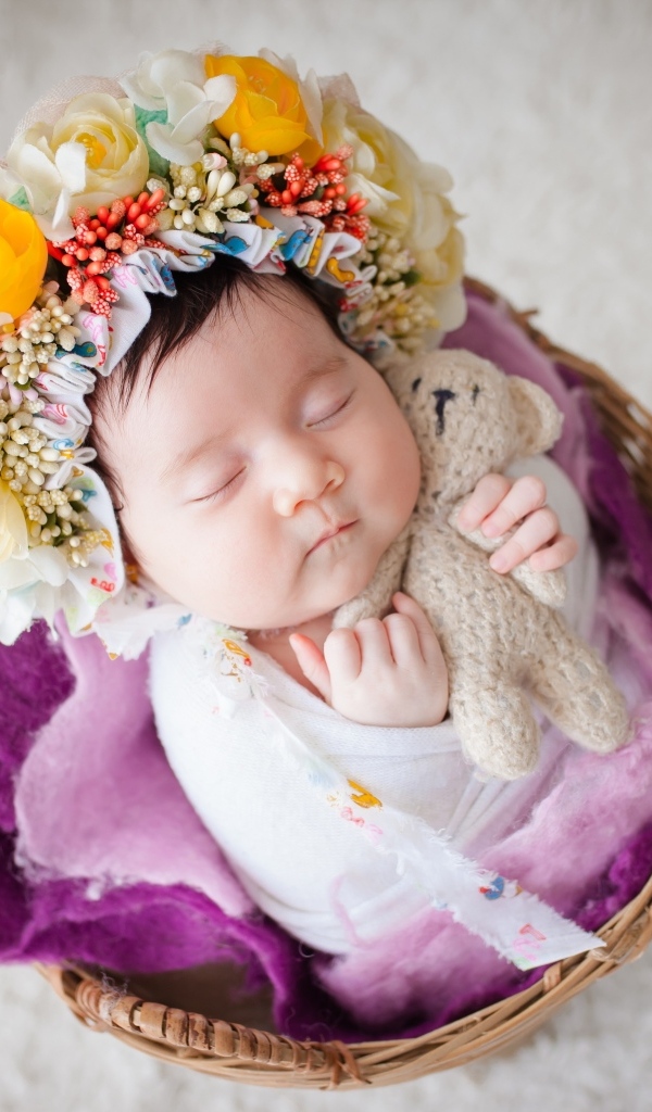 Новорожденная девочка с венком на голове спит в корзине