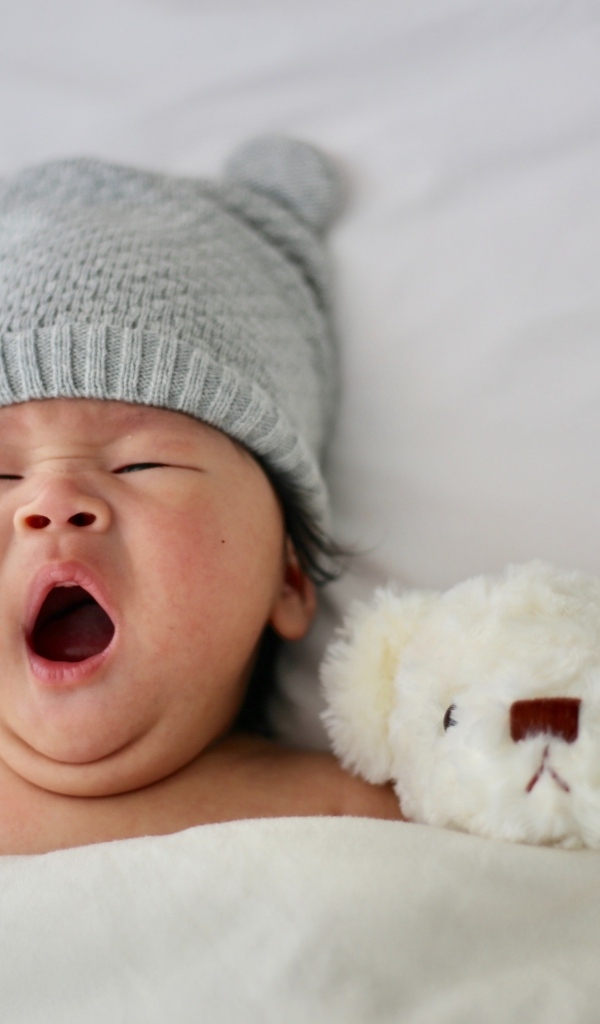 Новорожденный ребенок с игрушкой зевает в кровати