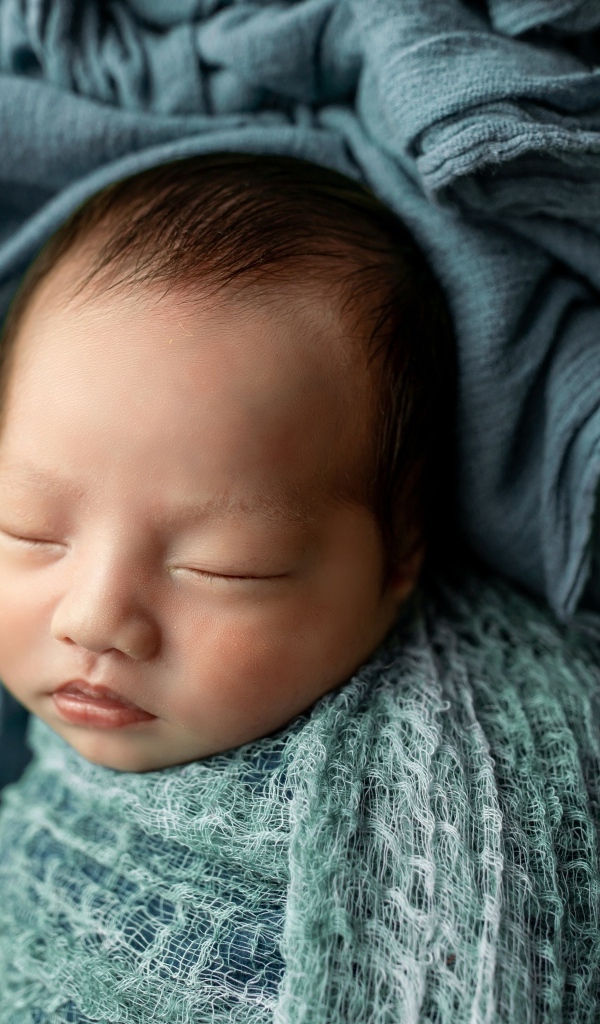 Новорожденный ребенок завернут в серое покрывало 