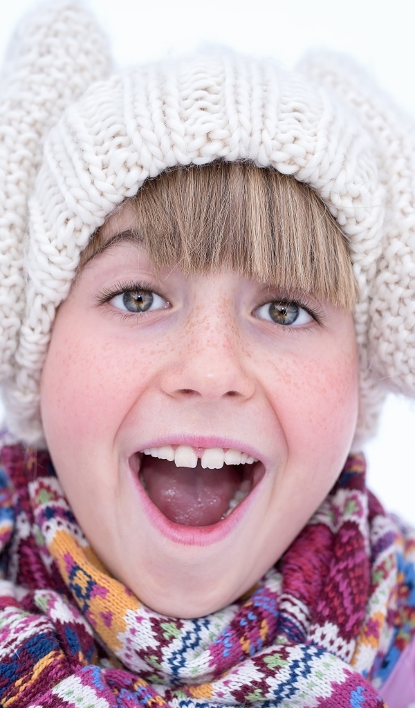 Довольная девочка в вязаной шапке и варежках